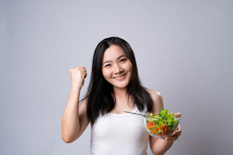 Portrait of a smiling young woman holding ice cream against white background