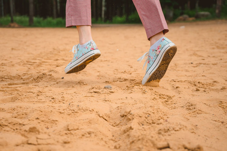 The legs of a girl in sneakers run along a sandy beach. sports recreation on the coast