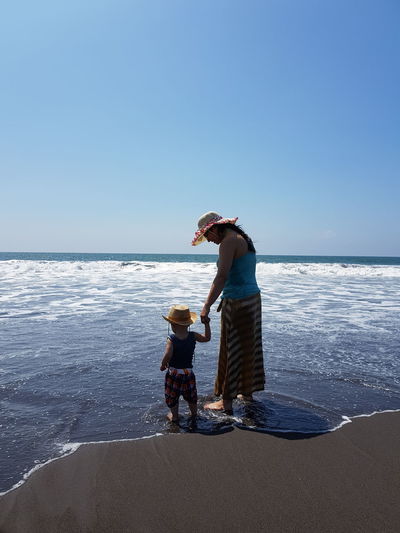 Mother and son standing on shore against blue sky