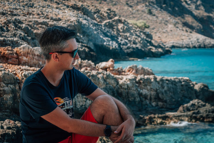 A man in sunglasses against the backdrop of rocks and the turquoise sea