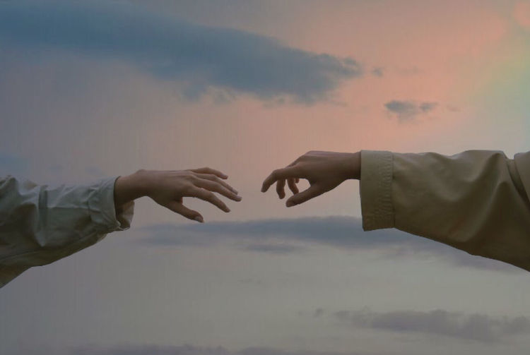 Cropped hands of people gesturing against sky during sunset