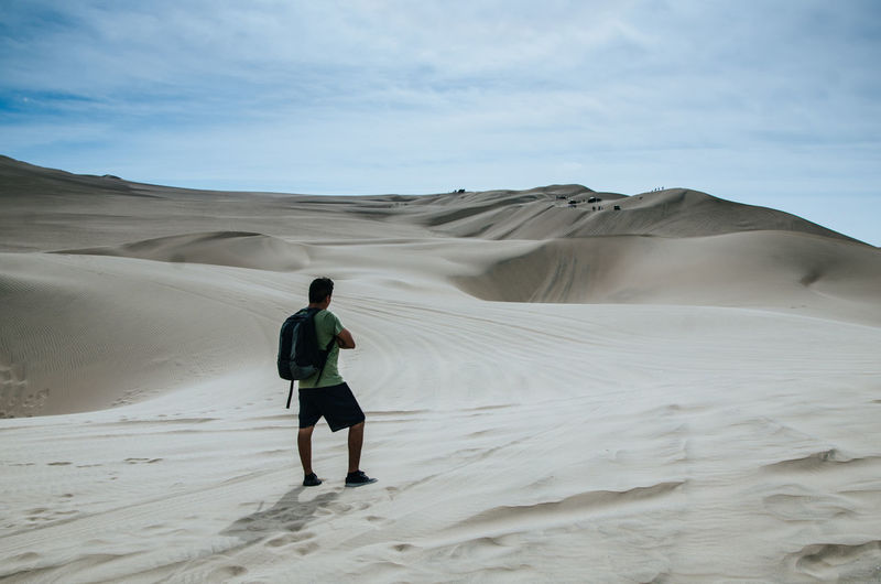 Rear view of man standing on sand dune in desert against sky