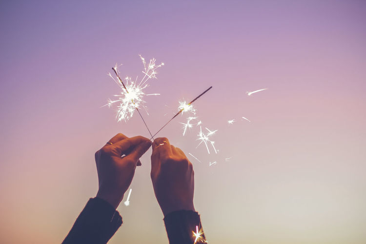 Close-up cropped hand holding burning sparklers at sunset