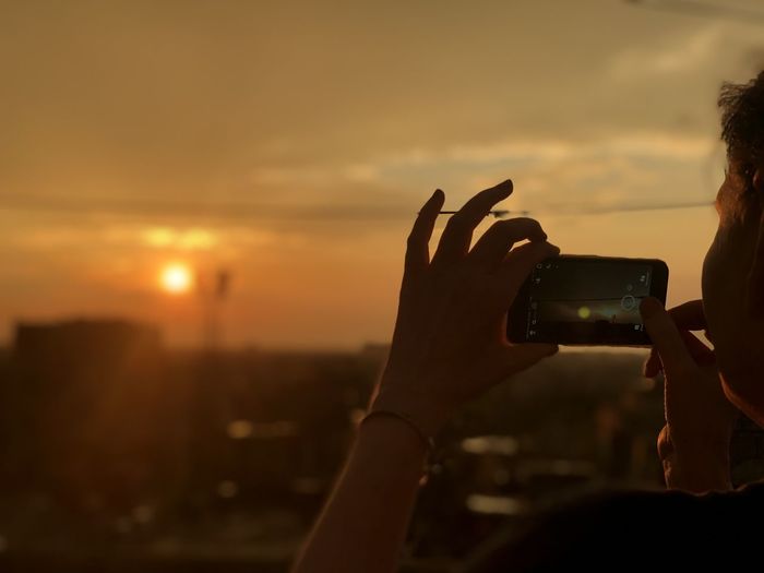 Midsection of woman photographing against sky during sunset