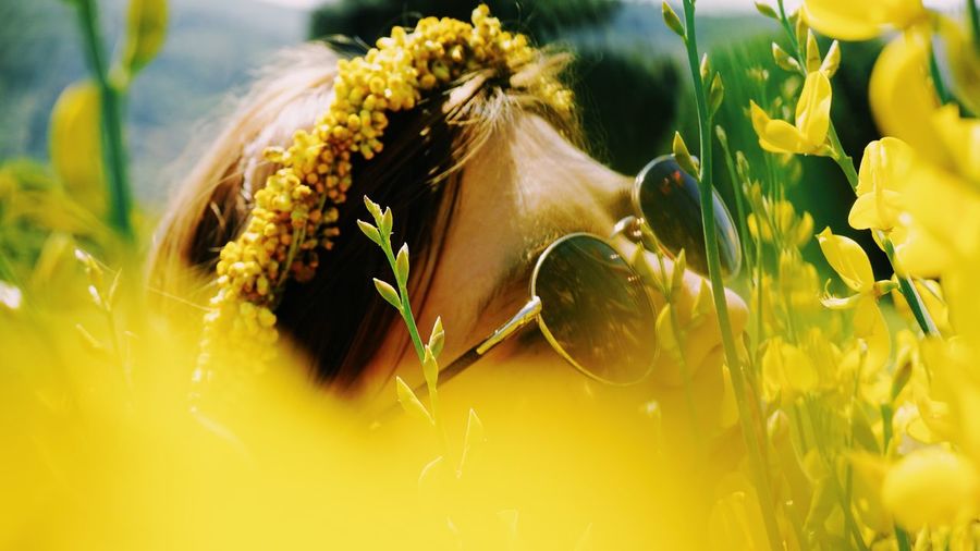 Close-up of woman wearing sunglasses amidst yellow flowers