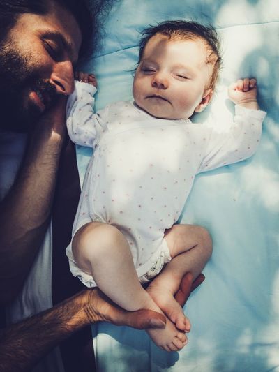 Directly above shot of shirtless father sleeping with toddler daughter on bed