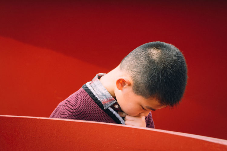 Boy looking away against red background