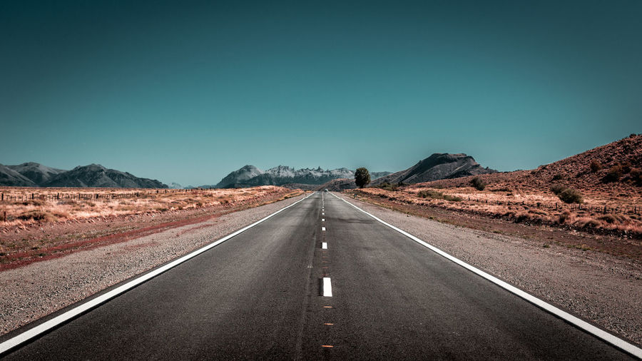 Road leading towards mountain against clear sky