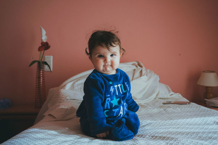 Portrait of boy sitting on bed at home