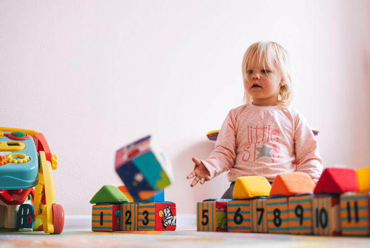 Little girl toddler in pink playing with blocks with numbers in children's room at home