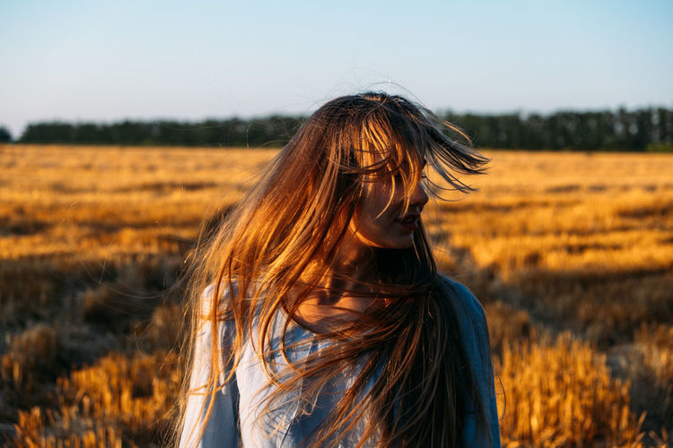 Peaceful woman with long hair in blue linen dress spending time in nature on summer day in sunset