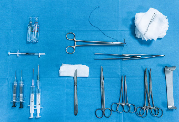 Top view of various stainless surgical tools and medical syringes arranged with flasks and napkins on blue background