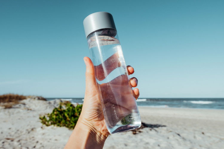 Female hand holding water bottle outdoor on sea shore health care concept for water balance. 