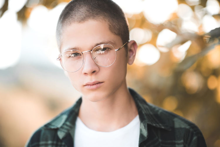 Teenage boy 16-18 year old wearing glasses outdoors over nature background. looking at camera. 