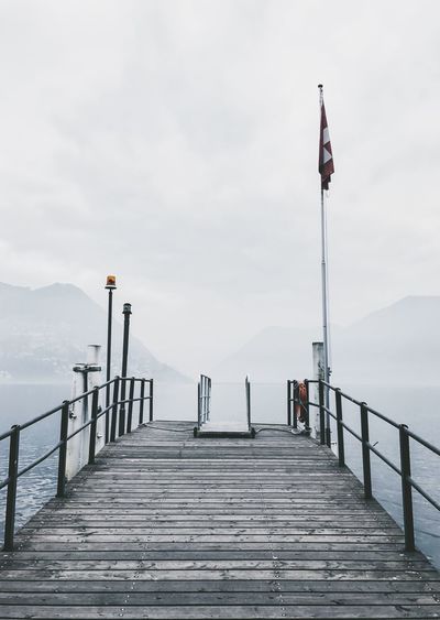Swiss flag on pier over lake against cloudy sky