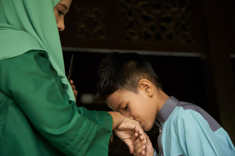 Profile view of malay son greeting and asking forgiveness to mother during ramadan festival 