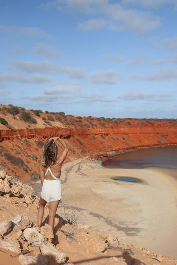 Pretty young blonde woman in white dress on cliff with red sandy beach on the west coast australia