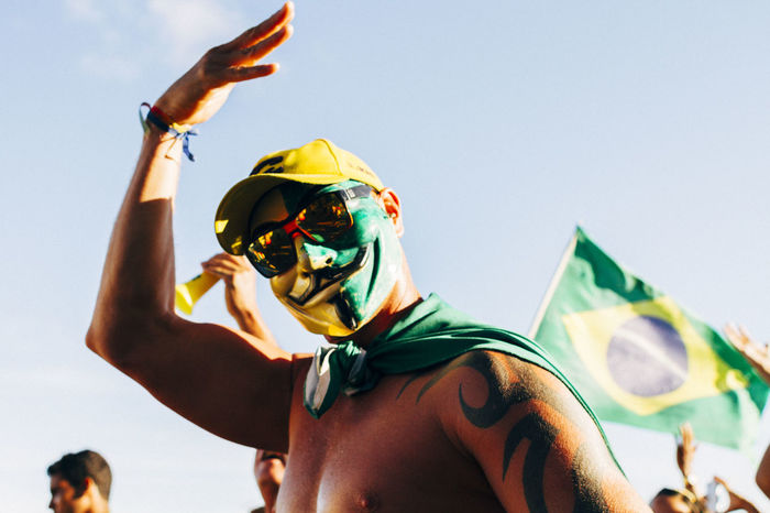 Low angle view of shirtless man with brazilian flag face paint against sky