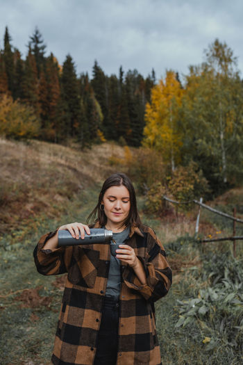 Portrait of smiling young woman standing on land with tea in thermos