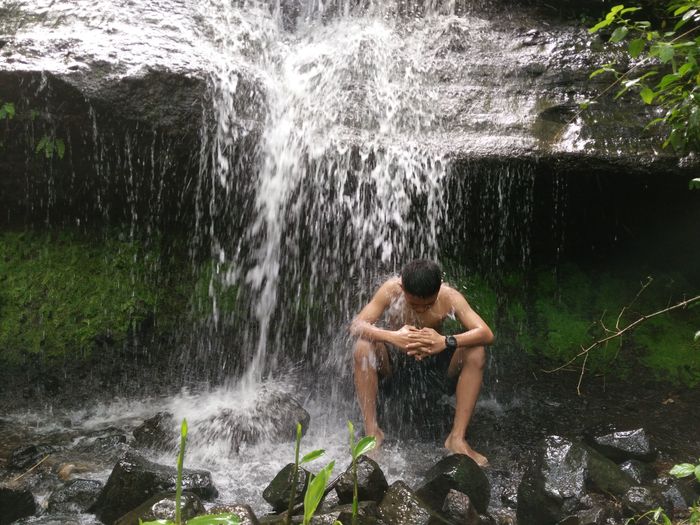 Full length of shirtless man splashing water in rock
