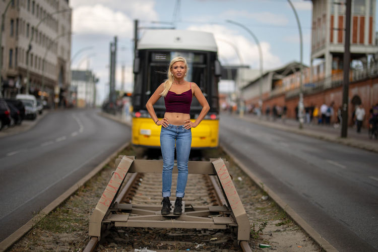 Portrait of stressed woman with hands on hip standing on railroad track against tram in city