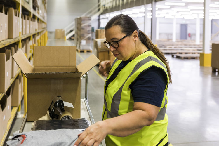Side view of female worker packing cardboard box at warehouse