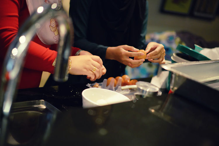 Cropped hands of people peeling boiled eggs in kitchen