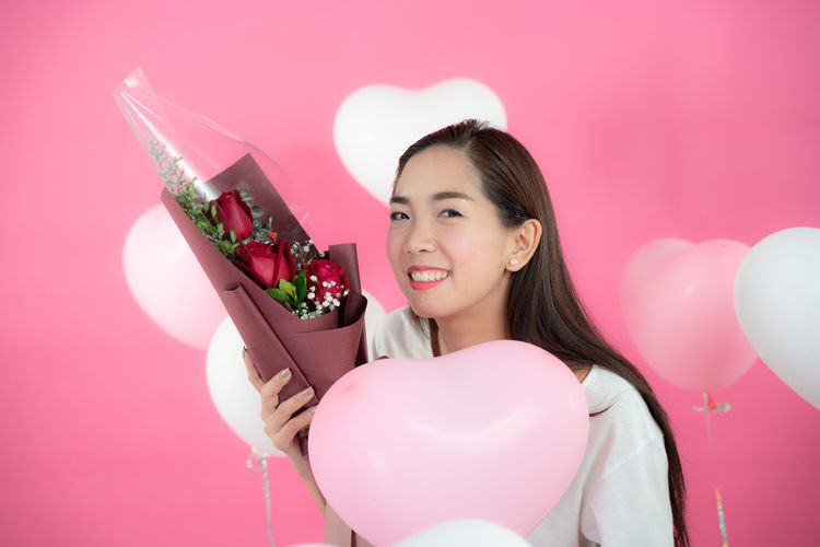 Portrait of a smiling young woman holding pink balloons