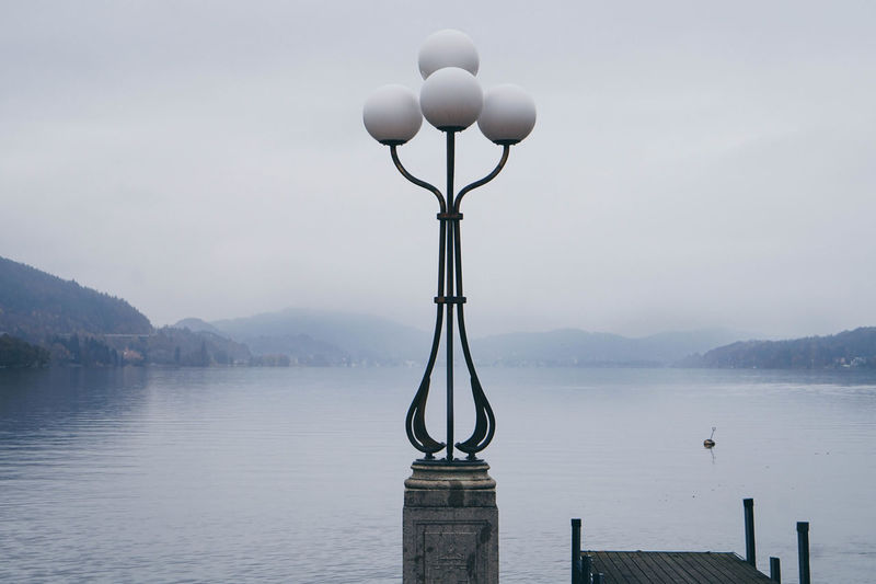 Electric lamp by lake against sky