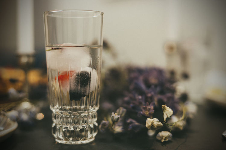 Close-up of water glass with berry ice cubes on table with dry flowers