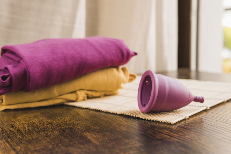 Menstrual cup on bamboo mat at table by colored clothes
