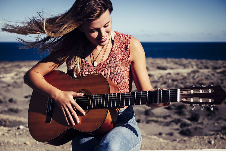 Smiling young woman playing guitar at beach