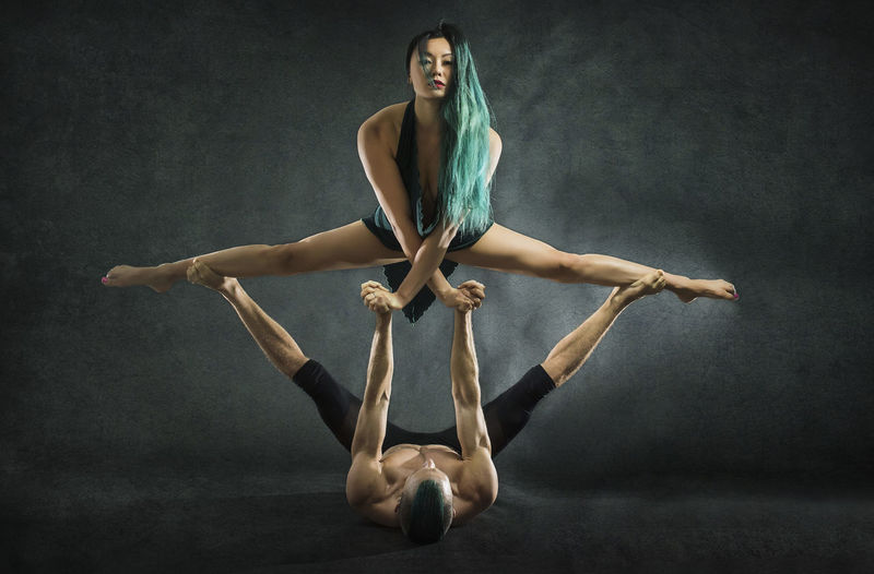 Young man and woman practicing acrobat against gray background