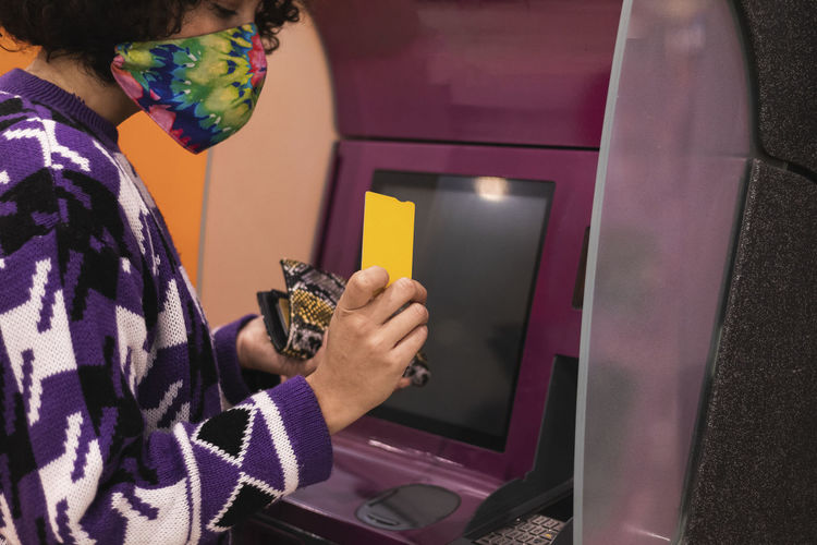 Young woman wearing face mask using credit card at atm