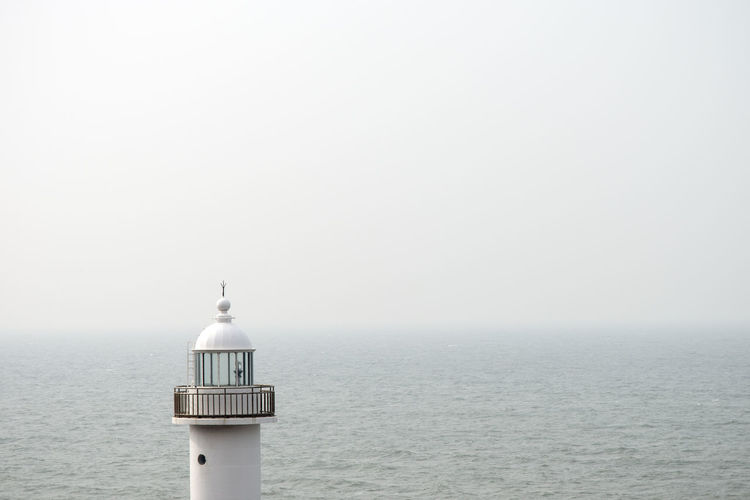 Lighthouse by sea against clear sky during foggy weather