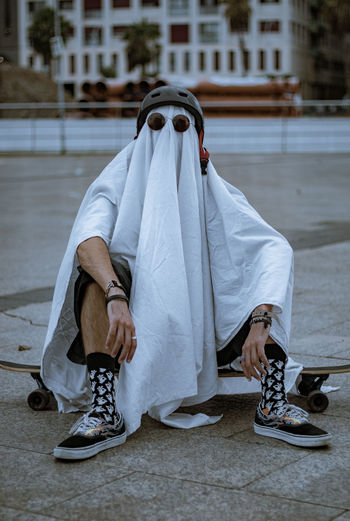 Rear view of a ghost costume doing skateboarding on street in city